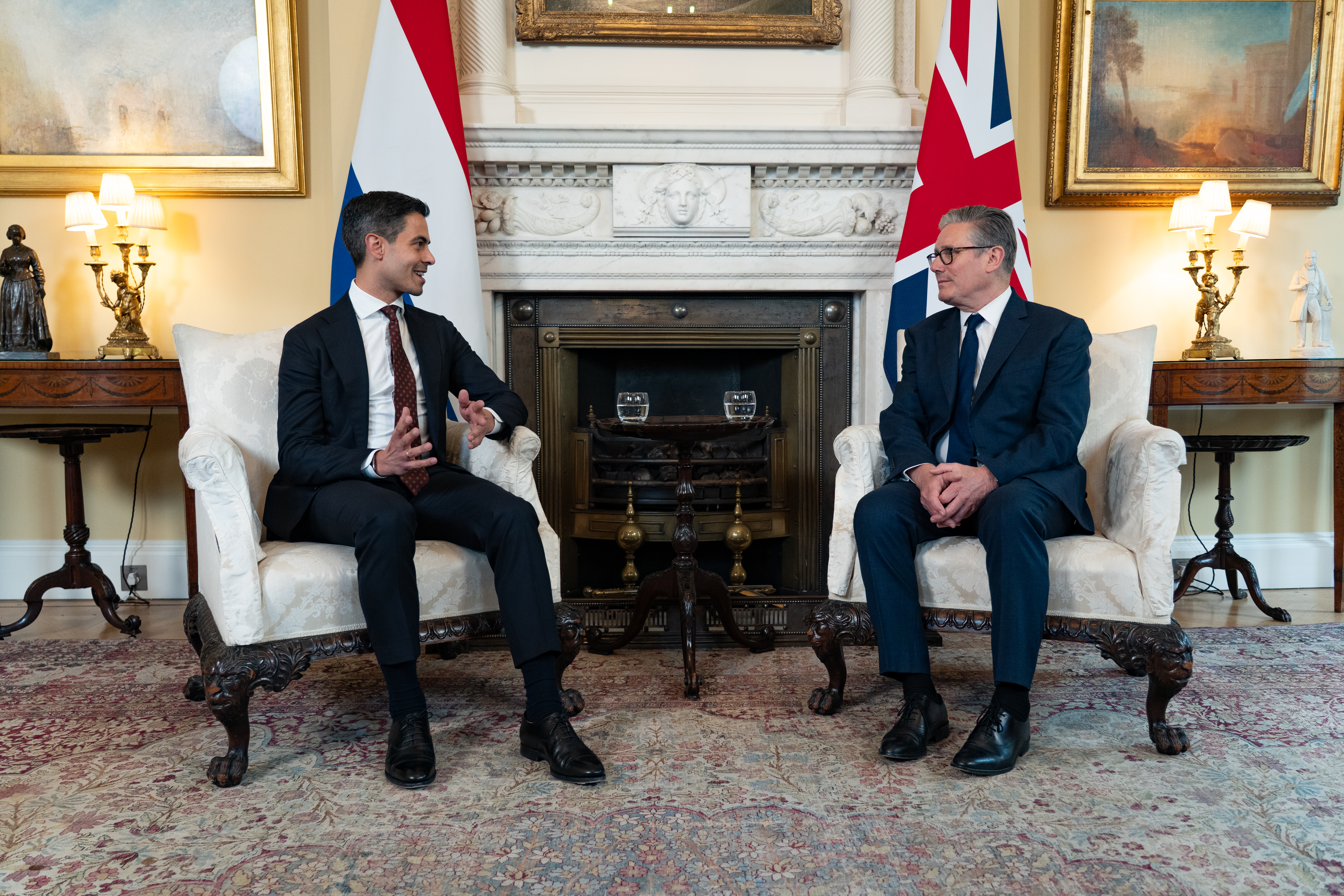 Prime Minister Rob Jetten sits with Prime Minister Keir Starmer in front of the Dutch and the British flag.