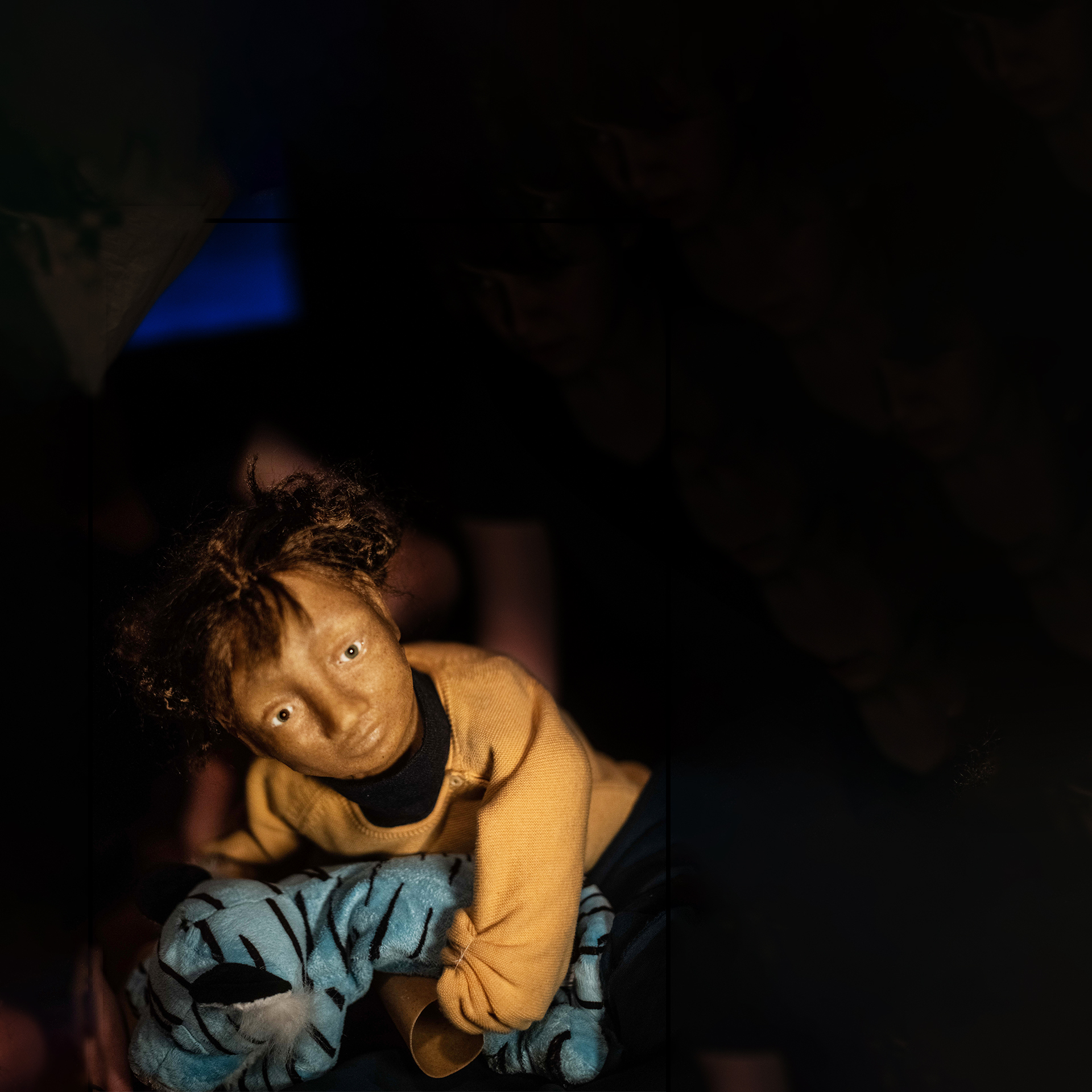 Photo of a puppet in the shape of a little girl dressed in dark yellow, carrying a blue stuffed tiger. Photo by Bert Grietens
